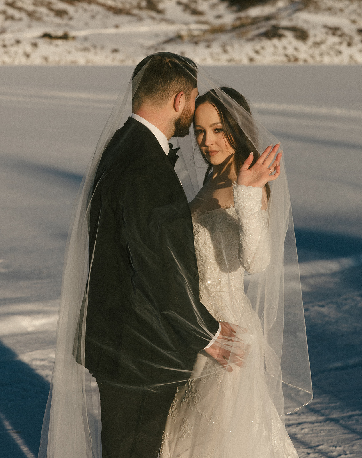 A bride and groom pose under the bride's veil in snowy Steamboat Springs, CO.