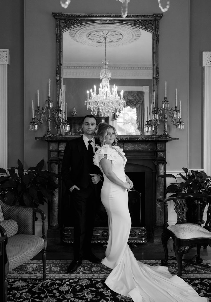 Black and white portrait of the bride and groom in the parlor at the Thomas Bennett House beside the fireplace, mirror and chandelier